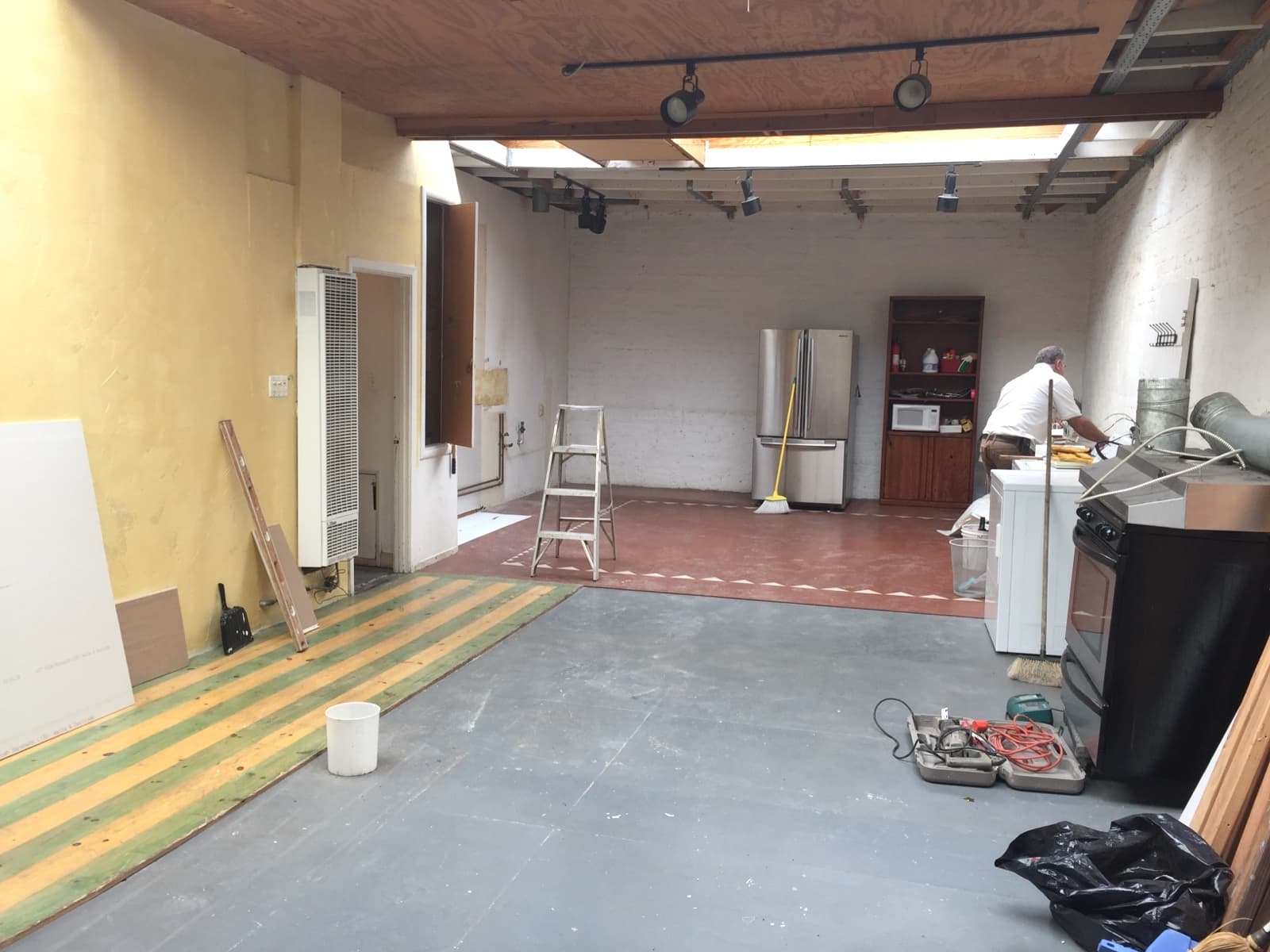 Wellness center before: the main room under a skylight with a grey floor, red tile, a fridge and track lights