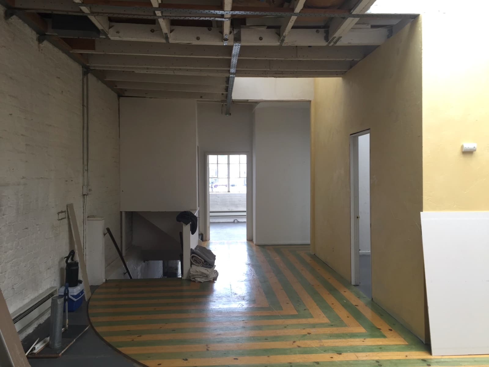 Wellness center before the fit-out: a floor striped green and bare wood, yellow walls and an open ceiling, looking toward the back rooms
