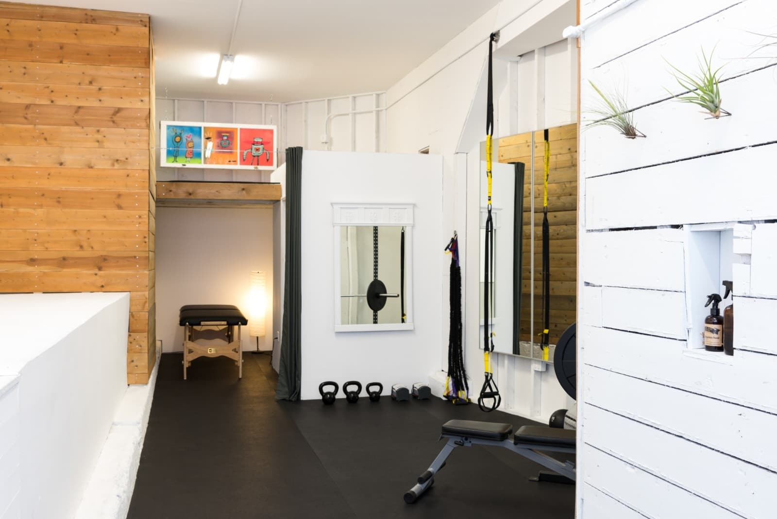 Guerrero Street studio after, looking toward the back wall: cedar plank wall, a white closet with a salvaged mirror, grey curtain, black rubber floor, kettlebells and a bench