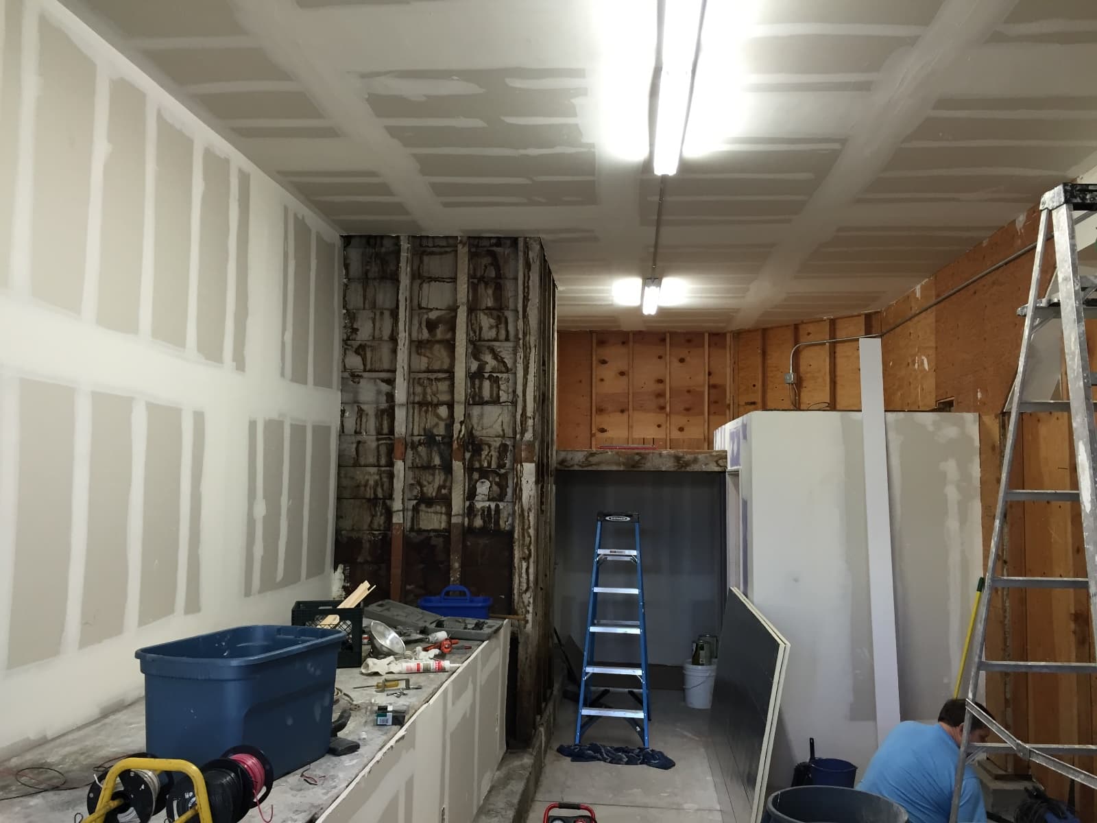 Guerrero Street garage mid-conversion, looking toward the back wall: fresh drywall and ceiling, a long built-in bench, a ladder in the open closet framing