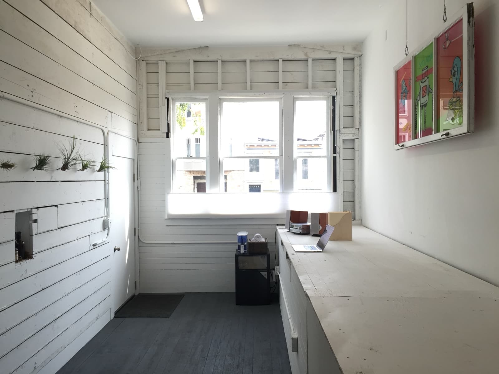Guerrero Street studio after, looking toward the street window: white shiplap walls, a long white bench and grey plank floor