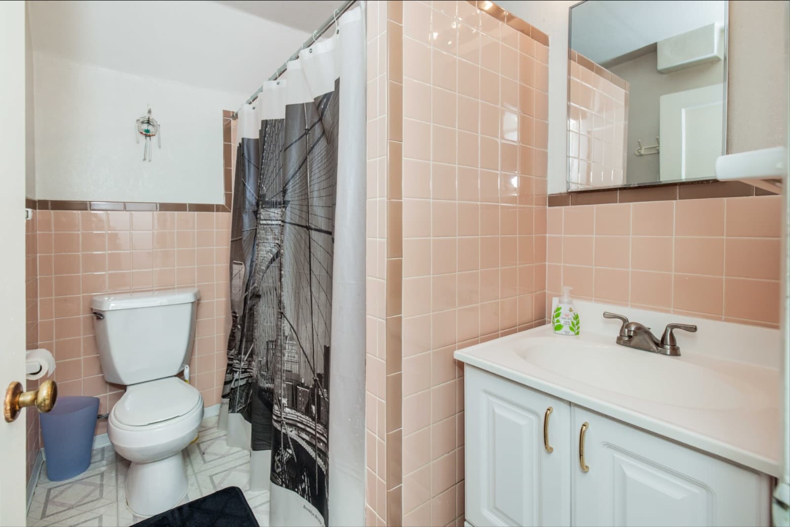 Corona Heights home downstairs bathroom before the remodel: pink wall tile, a white vanity, a toilet and a dark patterned shower curtain