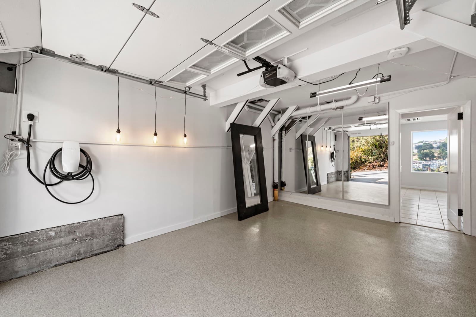 Corona Heights home garage after conversion: sealed grey floor, white walls, pendant lights and a mirror wall