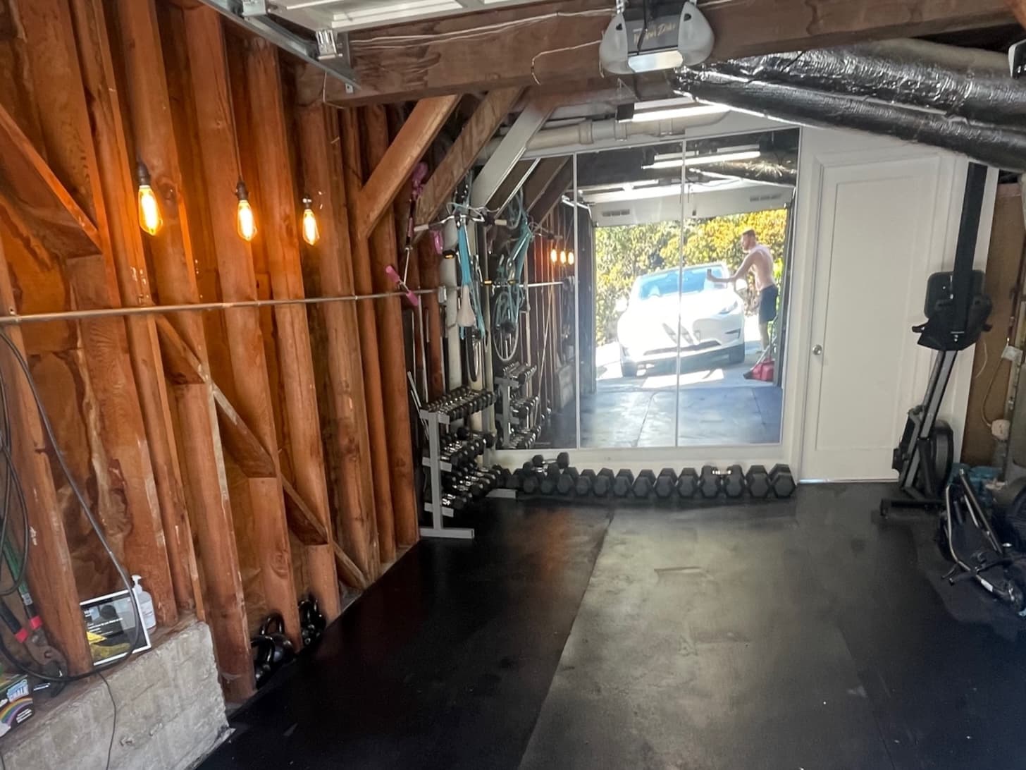 Corona Heights home garage before conversion: open studs, exposed ducts, a rubber mat on the floor and the garage door open to the driveway